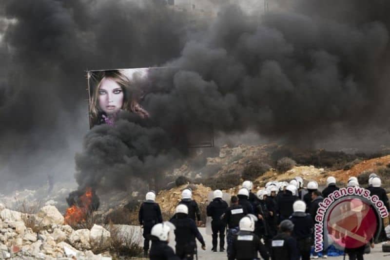 Polisi Palestina berjaga dekat ban yang dibakar oleh demonstran di kamp pengungsian Jalazoun dekat kota Ramallah, Tepi Barat.
