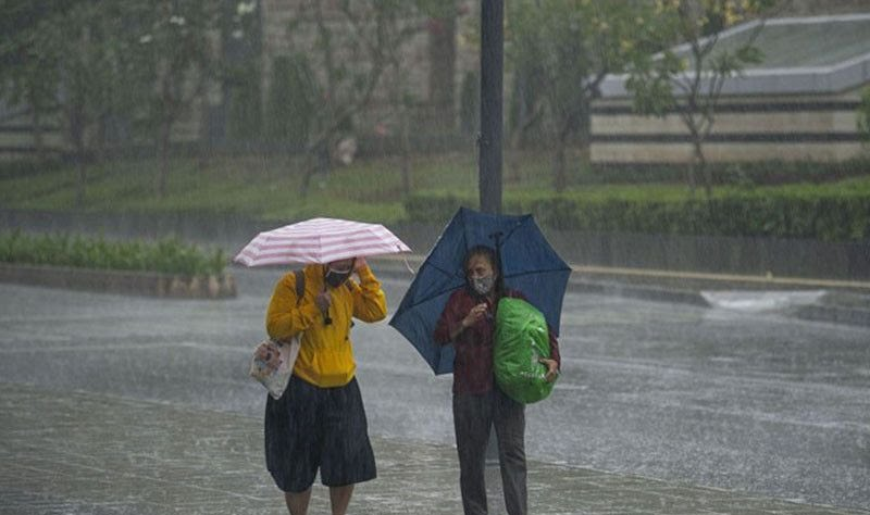 Warga memakai payung saat hujan lebat